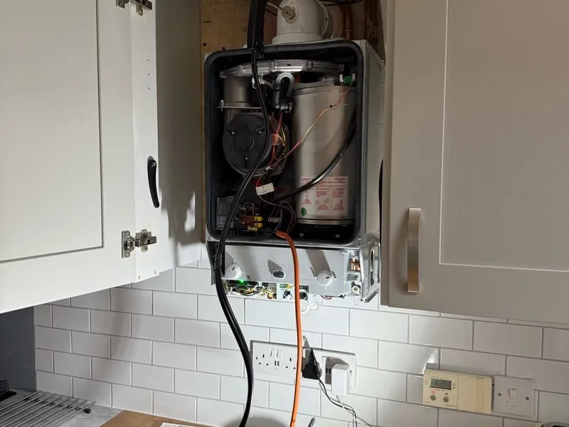 Boiler opened up for repair in a kitchen, controls and wiring exposed